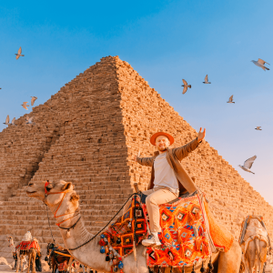 Hombre turista con sombrero montado en la pirámide de fondo de camello de Giza egipcia