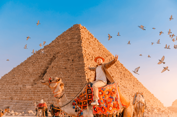 Hombre turista con sombrero montado en la pirámide de fondo de camello de Giza egipcia