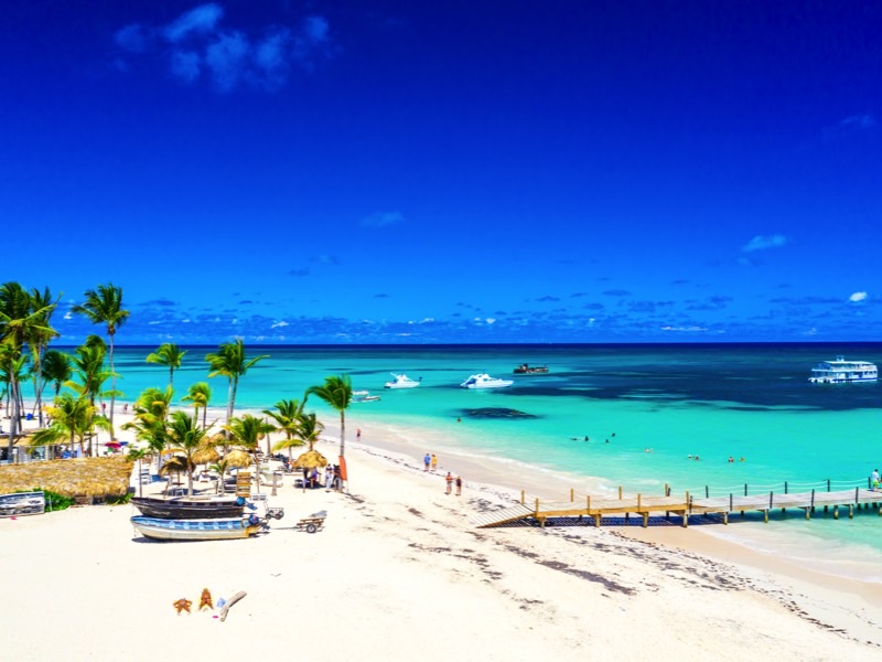 Aerial drone view of beautiful atlantic tropical beach with palms, straw umbrellas and boats. Bavaro, Punta Cana, Dominican Republic. Vacation background