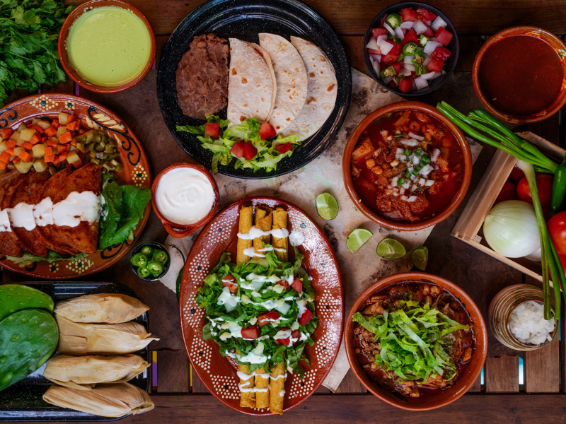 Mesa mexicana con menudo, pozole, enchiladas, tacos, salsa pico de gallo, flautas y tamales