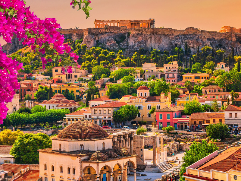 Skyline of Athens with Monastiraki square and Acropolis hill during sunset. Athens, Greece. Pink bougainvillea flower in the foreground.